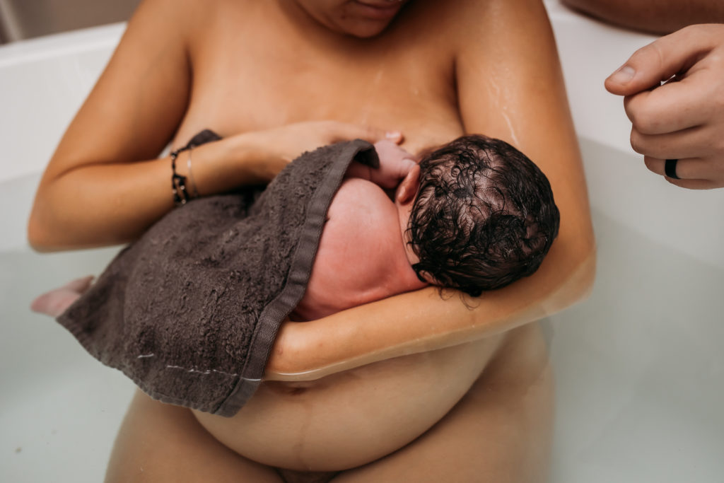 mom in bathtub after birth breastfeeding newborn